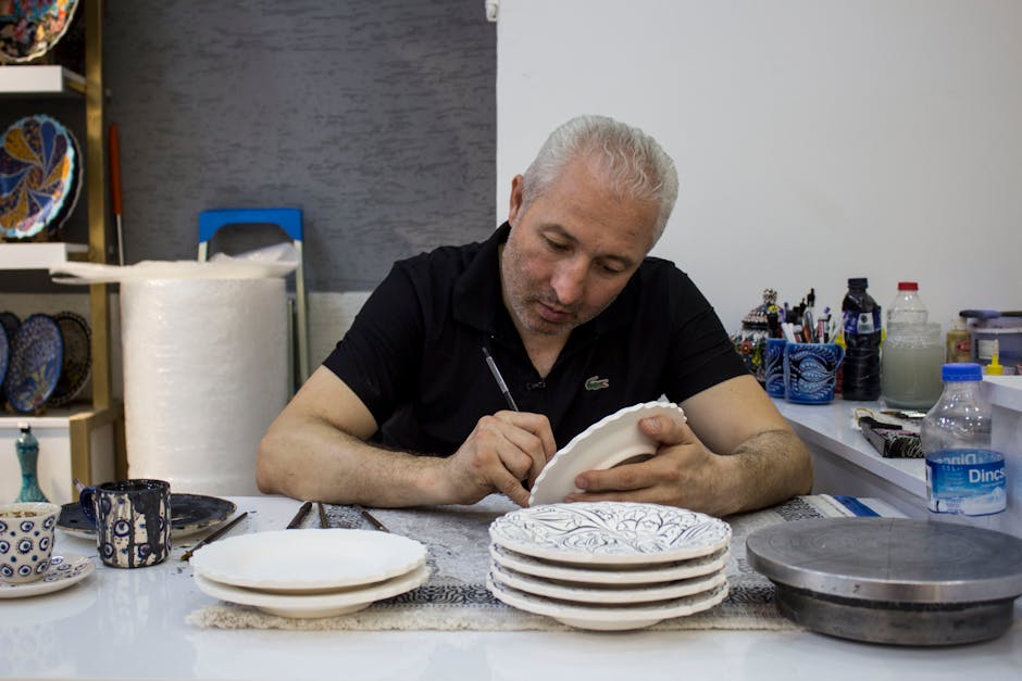 Man meticulously hand-painting intricate designs on ceramic plates in a studio setting.