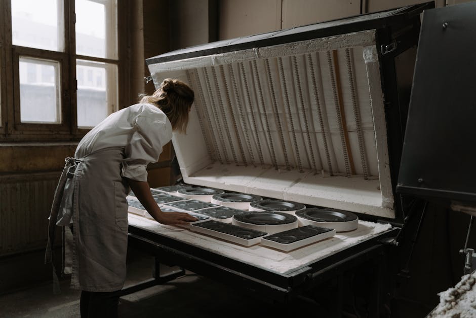 A female artisan carefully arranges ceramics in an industrial kiln, indicating precision and craftsmanship.