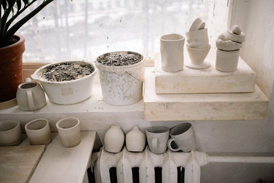 A collection of handcrafted pottery cups displayed on a window sill indoors, showcasing minimalist design.